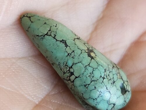 Polished Tibetan turquoise cabochon gemstone, 17 carats, featuring natural green color with black matrix veining, hand-cut and smooth rounded teardrop shape קבושון טורקיז טיבטי מלוטש, 17 קארט, בצבע ירוק טבעי עם פסי מטריקס שחורים, ליטוש ידני בצורת טיפה מעוגלת וחלקה